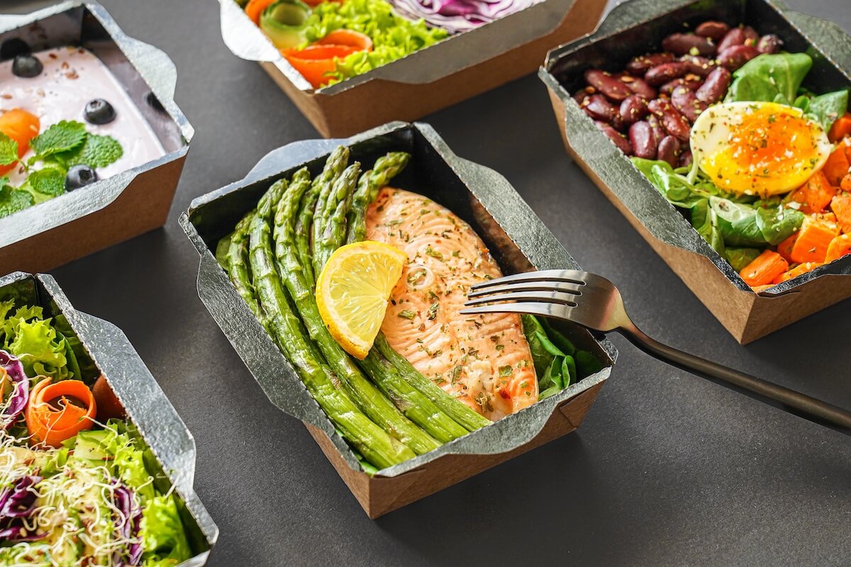 Salmon and asparagus healthy meal container next to other food containers.