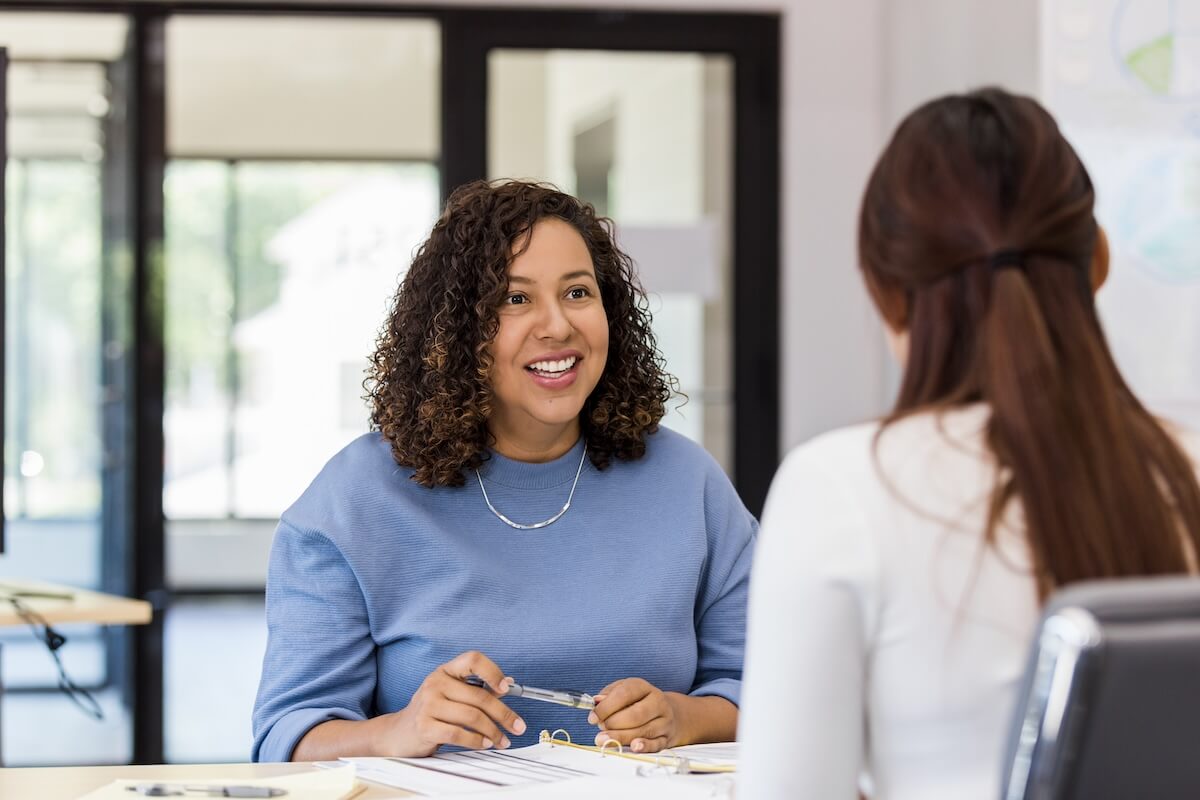 Woman sitting at desk as temporary staff helping another woman