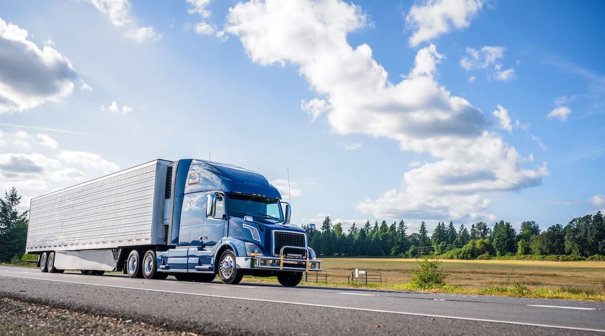 Shipping truck driving down highway passing empty field.