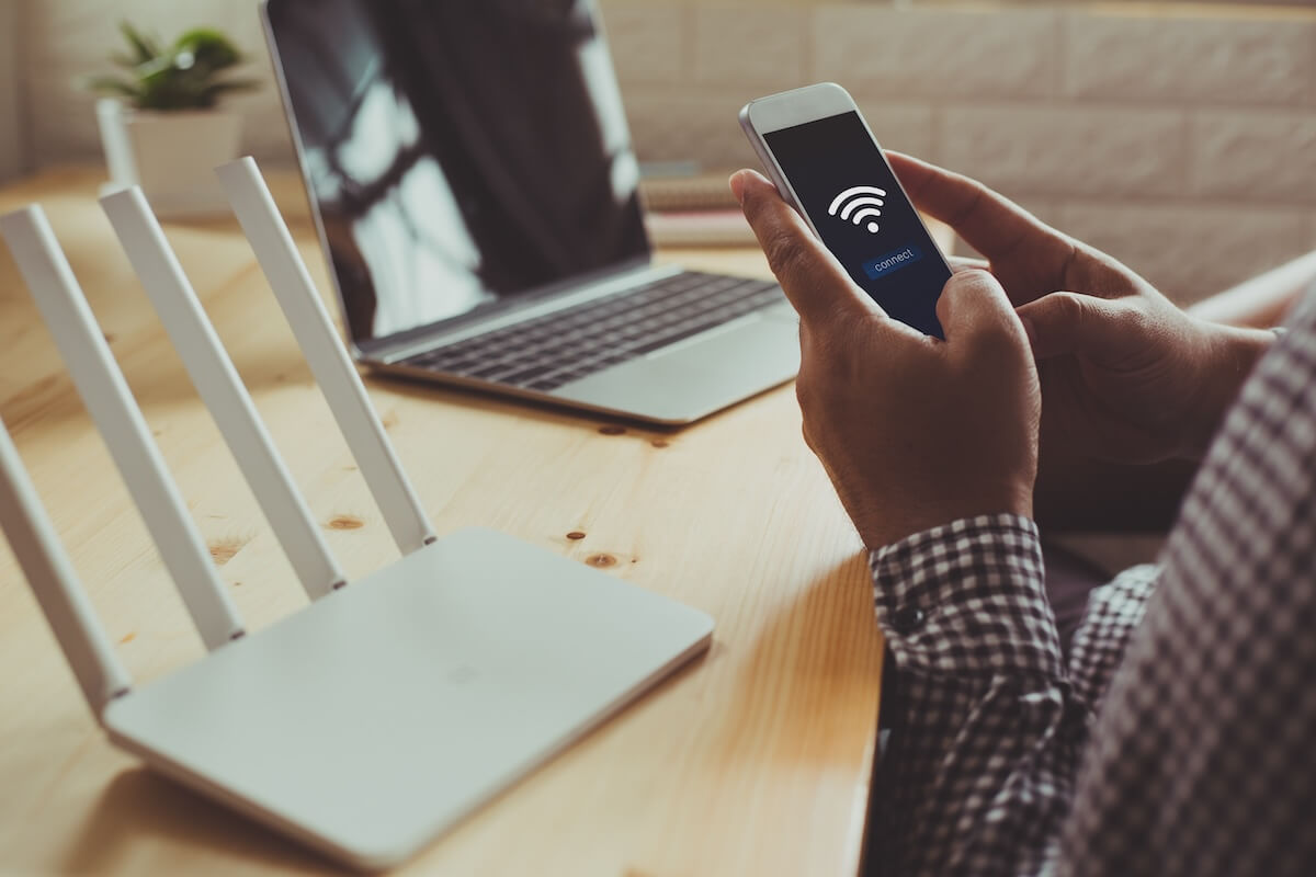 Person on phone connecting to the wifi device sitting next to them with laptop in background.